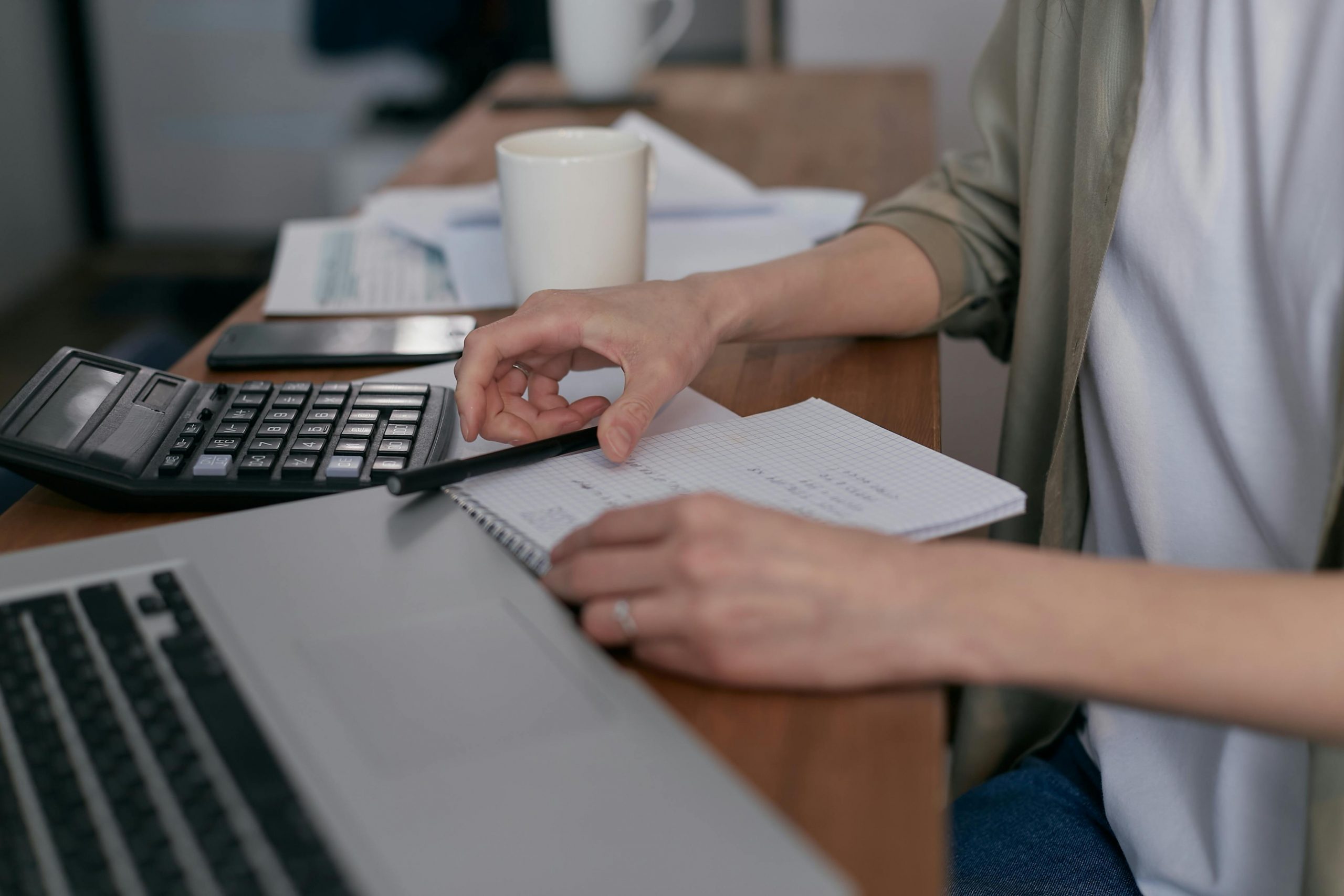 man using a calculator on a desk with a laptop